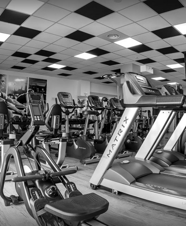 Salle de Sport Matrix : Rameur et Tapis de Course Modernes Intérieur de salle de sport moderne en noir et blanc, vue rapprochée sur un rameur Matrix et des tapis de course Matrix, avec un plafond à damier lumineux.